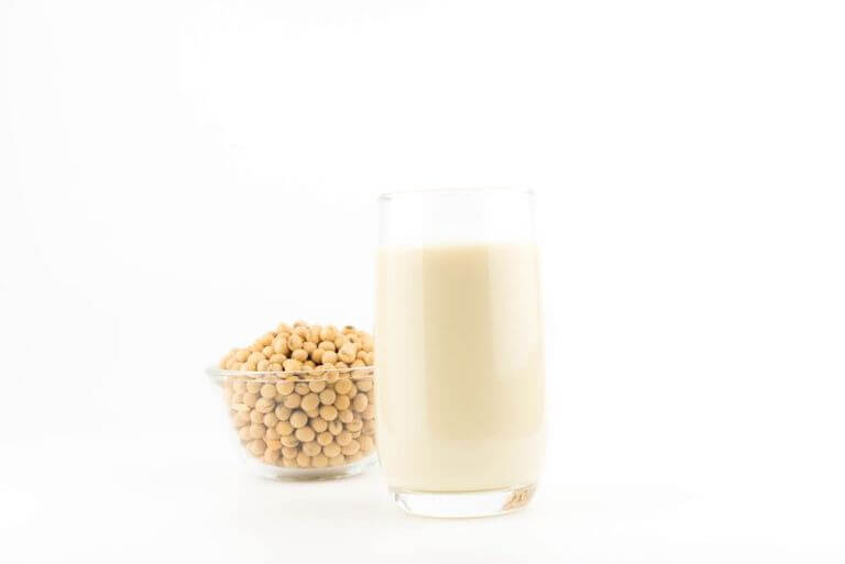 A glass bowl of soy nuts, and a glass of soy milk rest on a white background.