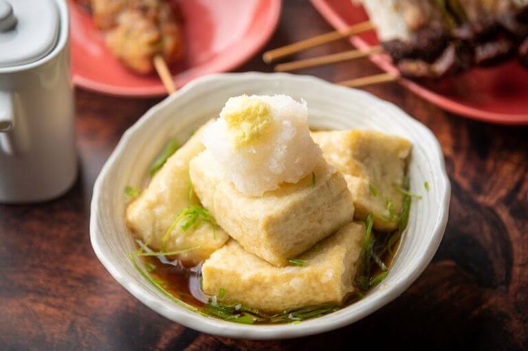 Five cubes of fried tofu rest in a white ceramic bowl with a thin, soy-based broth.