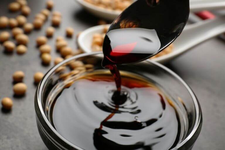 Soy sauce pours off a spoon into a glass bowl full of soy sauce.