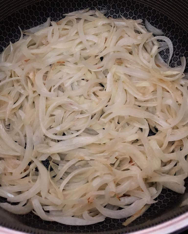 A closeup of onions caramelizing in butter in a non-stick pan