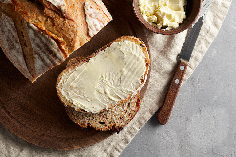 A creamy layer of butter is spread on a slice of bakery bread.