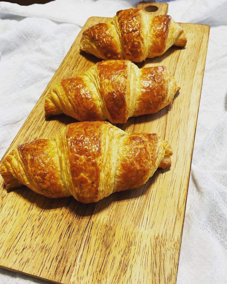 A perfectly baked trio of crescent-shaped croissants on a wooden plate.