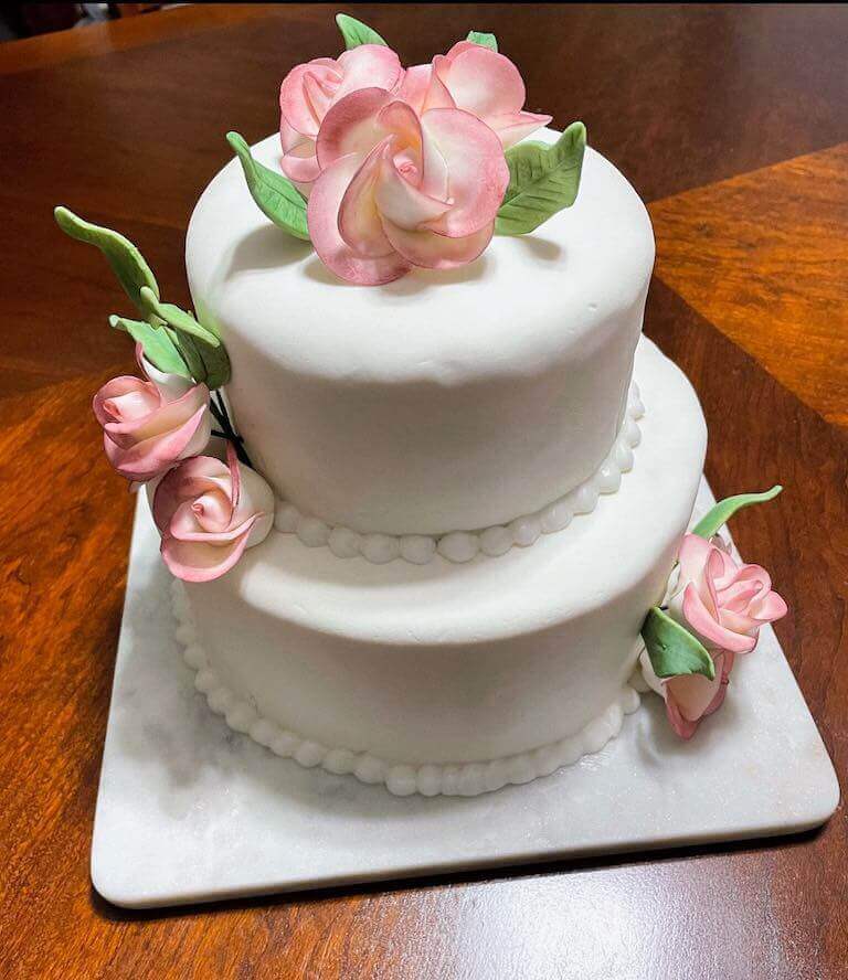 A cake decorated with simple white fondant and sculpted fondant flowers.