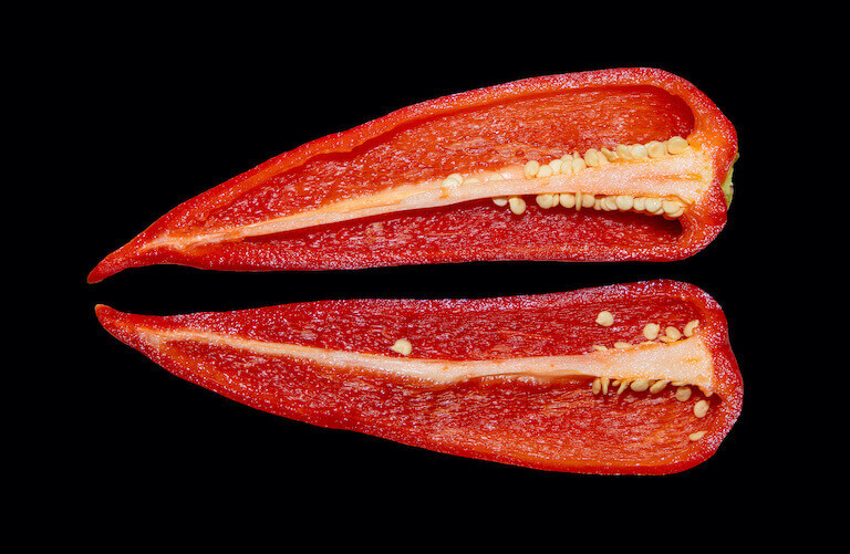 A red kapia pepper cut in two on a black background. 