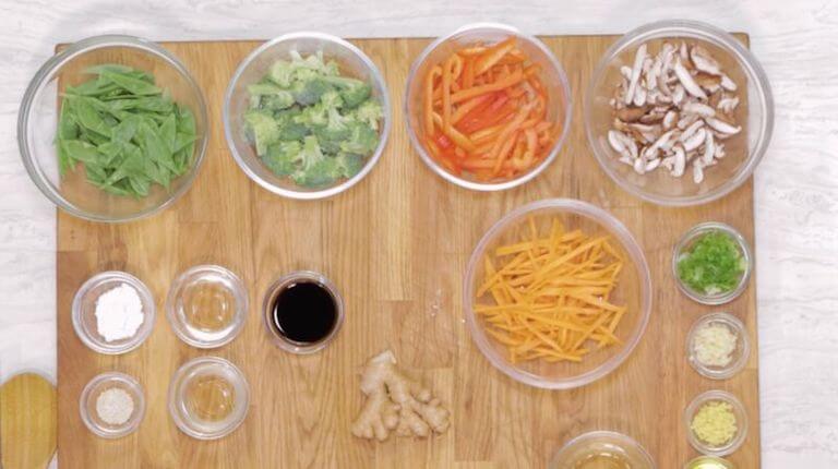 Carrots, ginger, and other ingredients for stir fry seperated into glass bowls on a counter