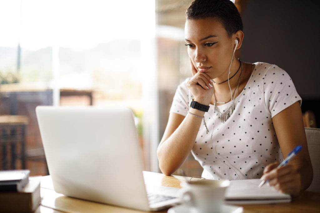  Studentessa che prende appunti mentre guarda il computer con gli auricolari