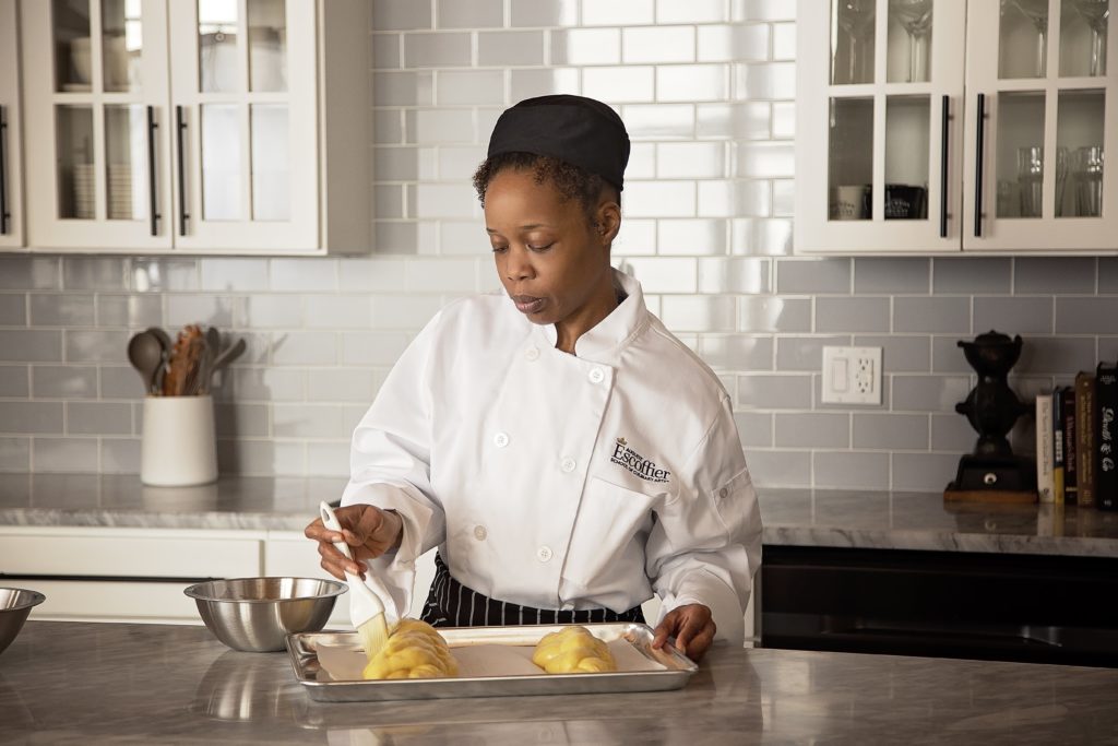 Female culinary student glazing dough in tray home kitchen