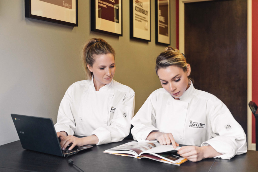  Deux femmes escoffier et chefs sur un ordinateur portable et un livre de lecture 