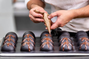 パイピングデコレーションチューブを使ってチョコレートの飾りを作るパティシエ