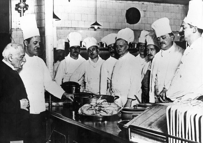 Auguste Escoffier and his kitchen staff standing at a table around a dish at The Carlton in London.