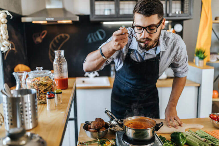 Home cook tasting soup from a pot in a kitchen.