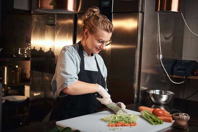 https://www.escoffier.edu/wp-content/uploads/2021/06/Smiling-chef-cutting-carrots-and-other-vegetables-on-a-white-cutting-board-in-a-kitchen-768.jpg