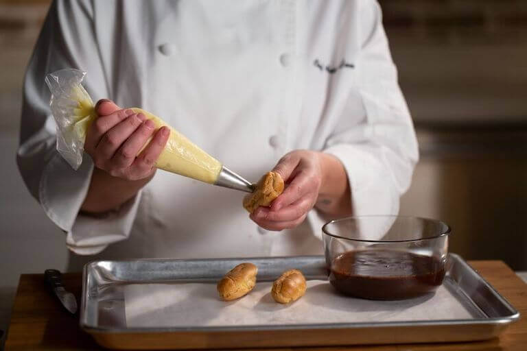 https://www.escoffier.edu/wp-content/uploads/2021/07/Chef-filling-eclairs-with-pastry-cream-768.jpeg