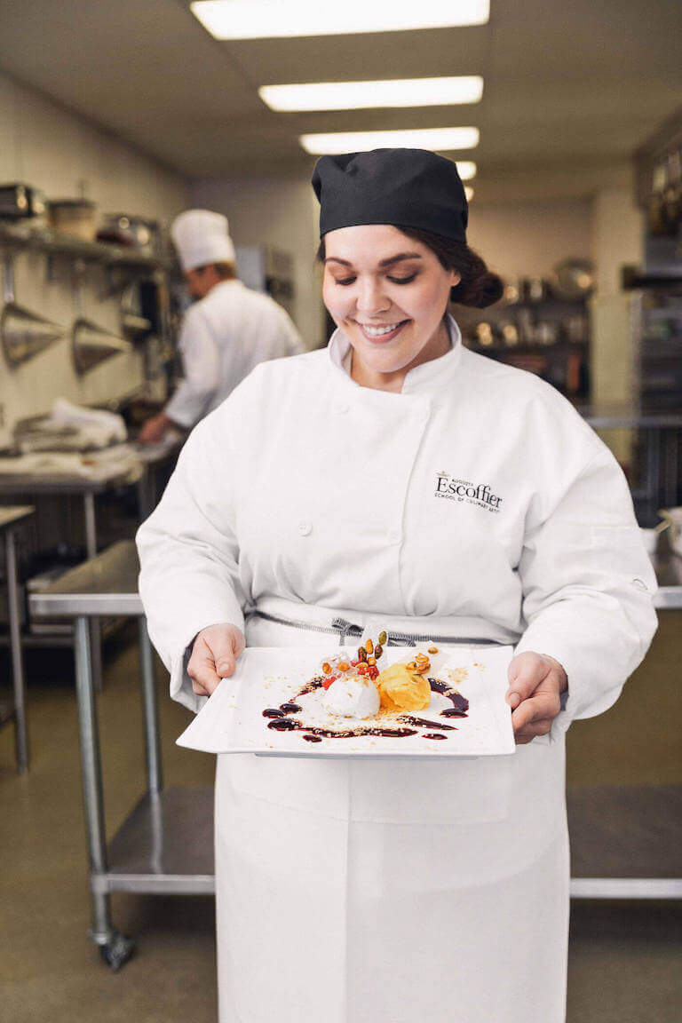 Smiling Escoffier student holding a white plate with dessert.