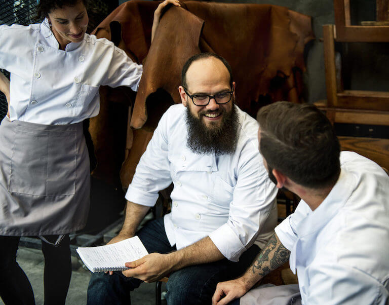 Smiling male chef with beard and glasses holding a journal.