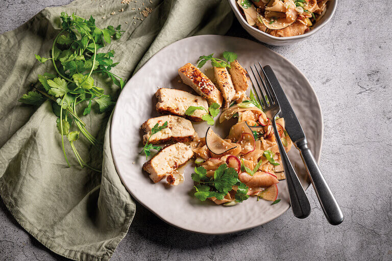 Six slices of sous vide chicken are arranged on a plate with a side of pickled turnips and cilantro garnish.