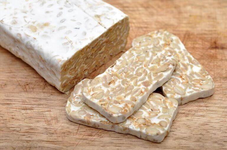 A block of plain tempeh sits on a wooden cutting board, with three slices of tempeh cut off.