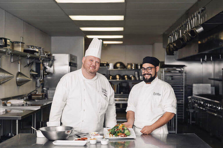 Escoffier chef instructor and smiling male culinary student with mixed vegetable plate