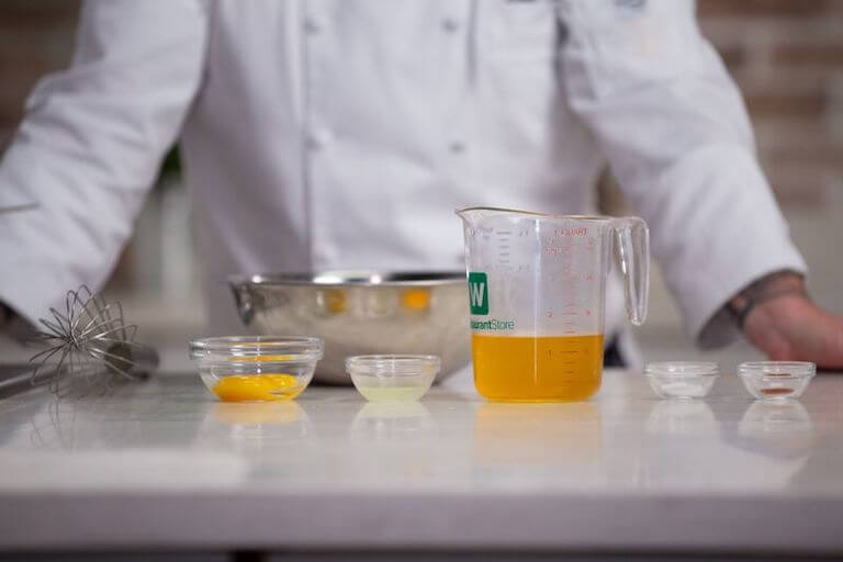 Escoffier instructor demonstrates mise en place for a sauce recipe, with small containers of ingredients in front of him on a countertop.