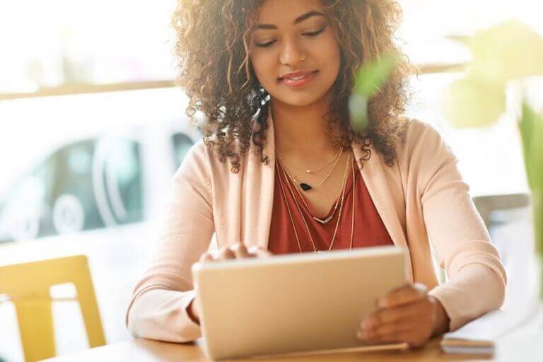 A young woman is holding a tablet and doing online work in a cafe setting.