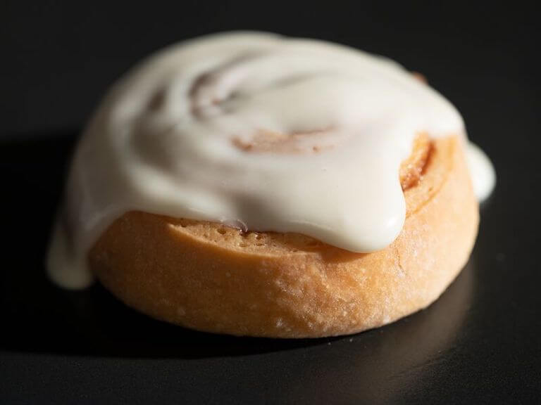 Close-up view of a cinnamon bun with icing against a black background.