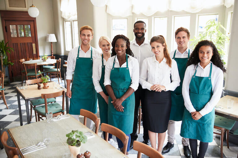 Restaurant employees in green aprons standing in a restaurant