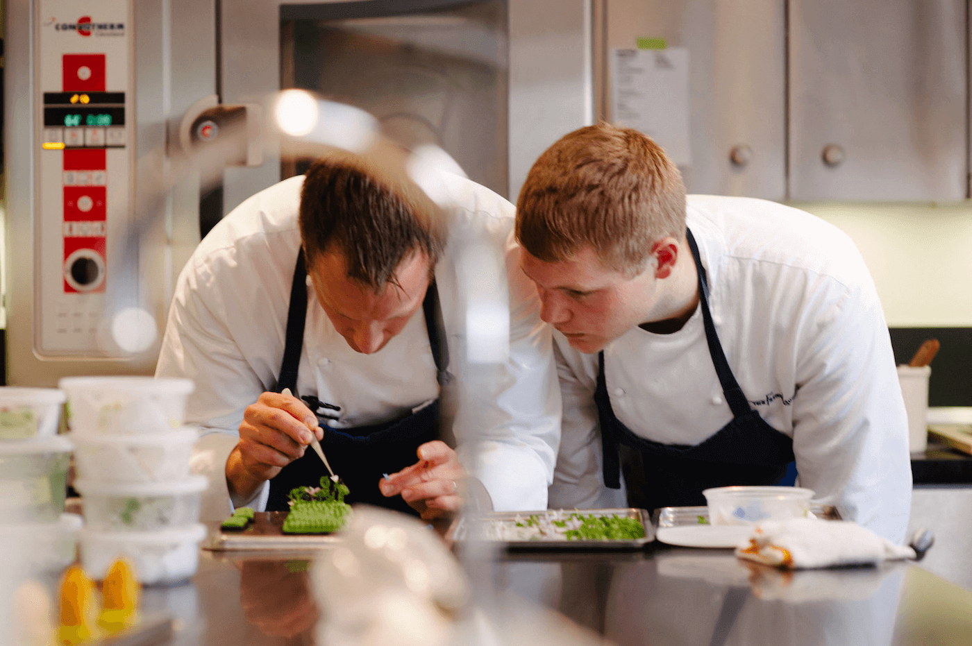 https://www.escoffier.edu/wp-content/uploads/2022/10/Two-chefs-leaning-over-a-kitchen-counter-while-one-chef-places-a-small-flower-detail-on-a-plate-with-tweezers-1400.png