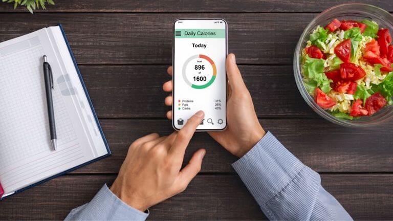 A person uses a calorie-tracker app on a smartphone to log a salad meal.