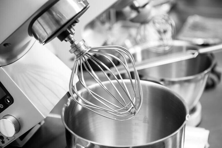 A close-up photo shows a stainless steel, professional-grade stand mixer with a whisk attachment.