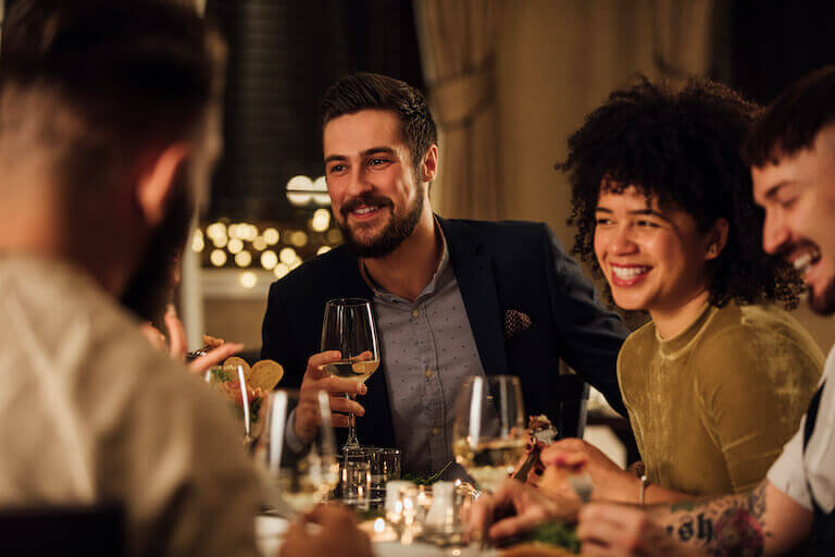 A group of well-dressed friends laughing and chatting casually over glasses of wine in a restaurant dining room.