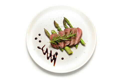 Lamb medallions and asparagus garnished with rosemary on a white plate