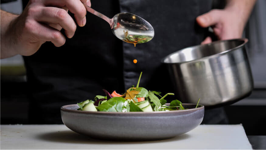 A chef drizzles dressing on a fresh garden salad in a stone bowl
