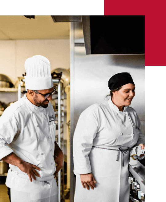 An Escoffier Boulder campus culinary arts Instructor watching a student cooking in a classroom kitchen