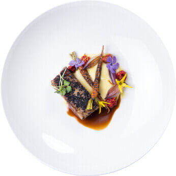 A gourmet plated restaurant dish of tuna with carrots and edible flowers