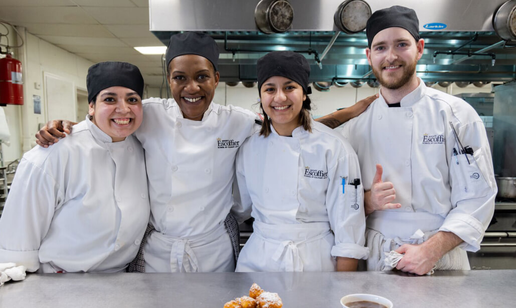 A group of four Escoffier Austin culinary students wearing chef coats smiling mobile view