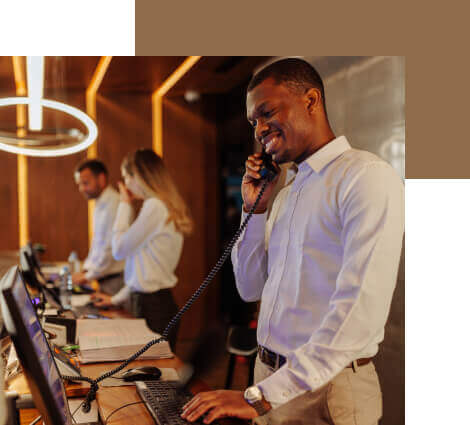 a hotel manager talks on the phone with a guest at a hotel reception desk