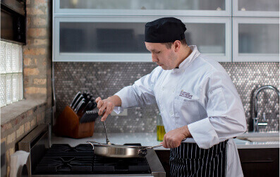 An Escoffier online student stirring vegetables in a frying pain in his home kitchen