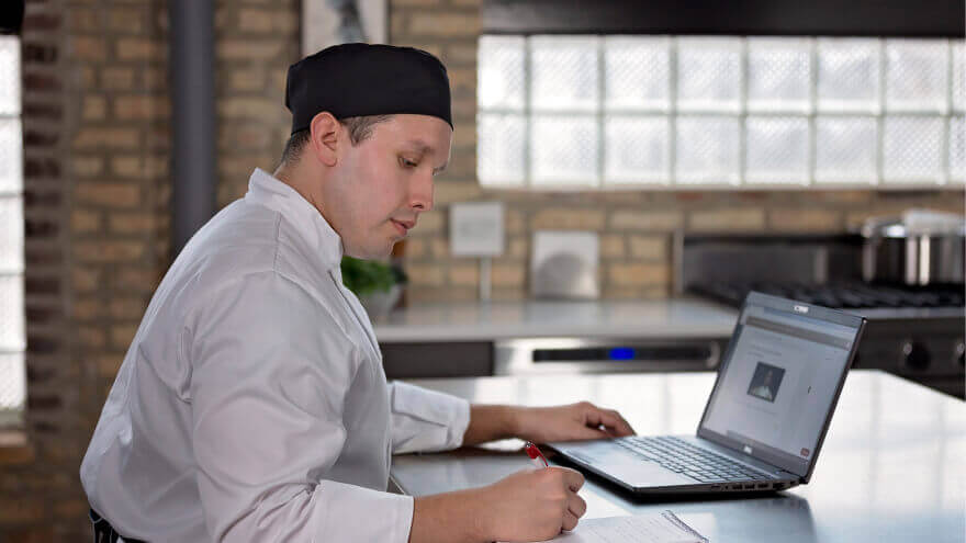 An Escoffier online student takes notes in front of his laptop computer