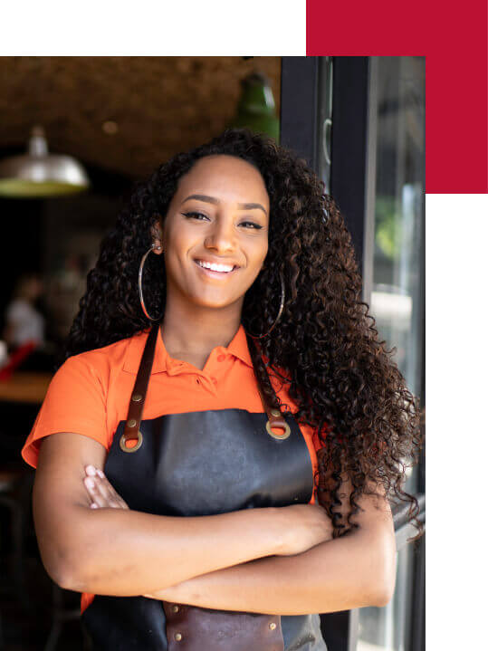 A female chef stands with her arms crossed in the door of her restaurant