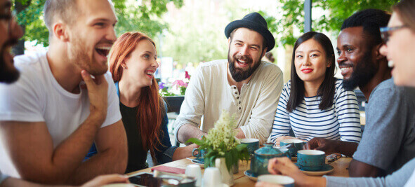 A diverse group of friends laugh while dining at an outdoor restaurant