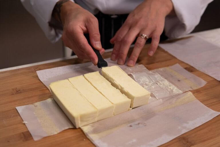 Four sticks of margarine have been cut from a single large block and rest on a piece of wax paper.