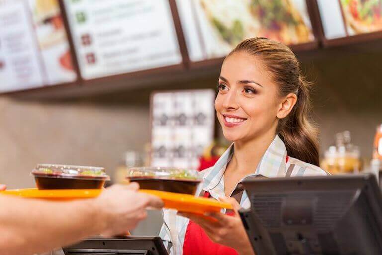 Restaurant worker serving two fast food meals on a tray with a smile.