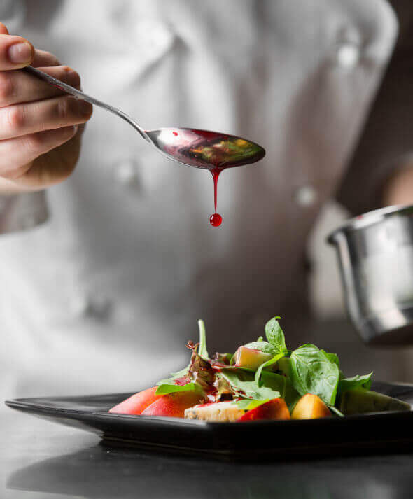 A chef finishes a gourmet restaurant dish with a demiglace