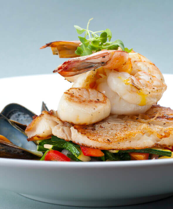 A close-up of a restaurant seafood dish with shrimp, scallops, fish, and vegetables