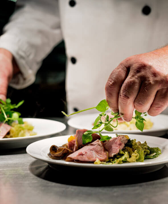 A male chef finishes a gourmet restaurant plate with herbs