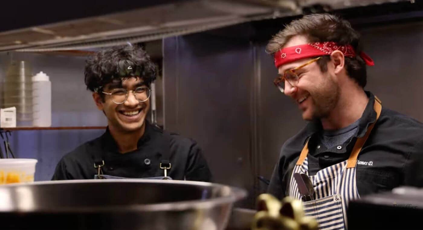 An Escoffier student smiling with a chef in a kitchen at a restaurant where he is doing his industry externship
