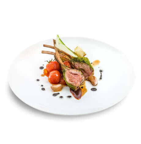 A rack of lamb with tomatoes, roasted garlic, and sauce on a white plate