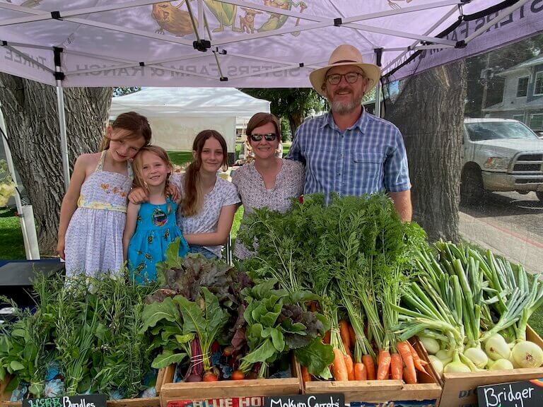 Escoffier Boulder campus Chef Instructor Steven Nalls stands with his wife and three daughters at their farm stand full of green vegetables.