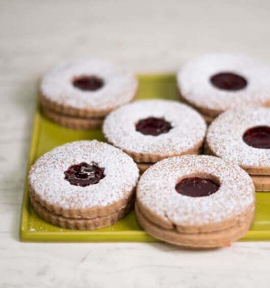 A close up of Linzer cookies with raspberry filling and powdered sugar on a square lime green plate