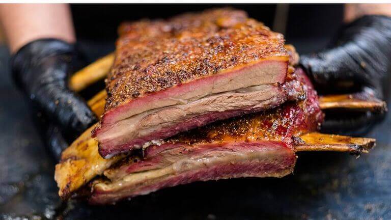 A chef holds a rack of beef ribs that are cut open to show the perfectly cooked meat.